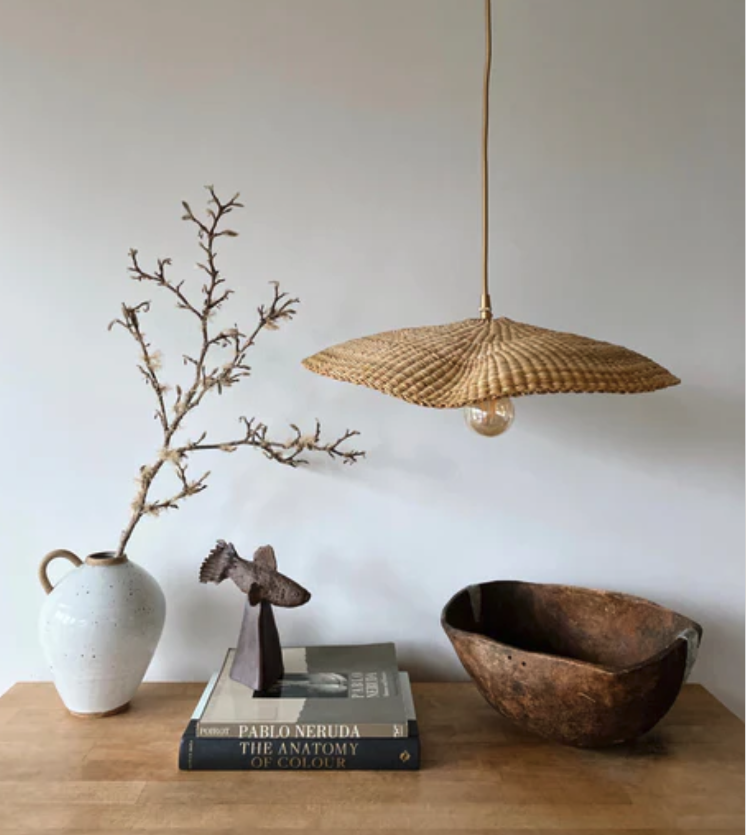 Close-up of a woven rattan light paired with ceramic vases and art books.