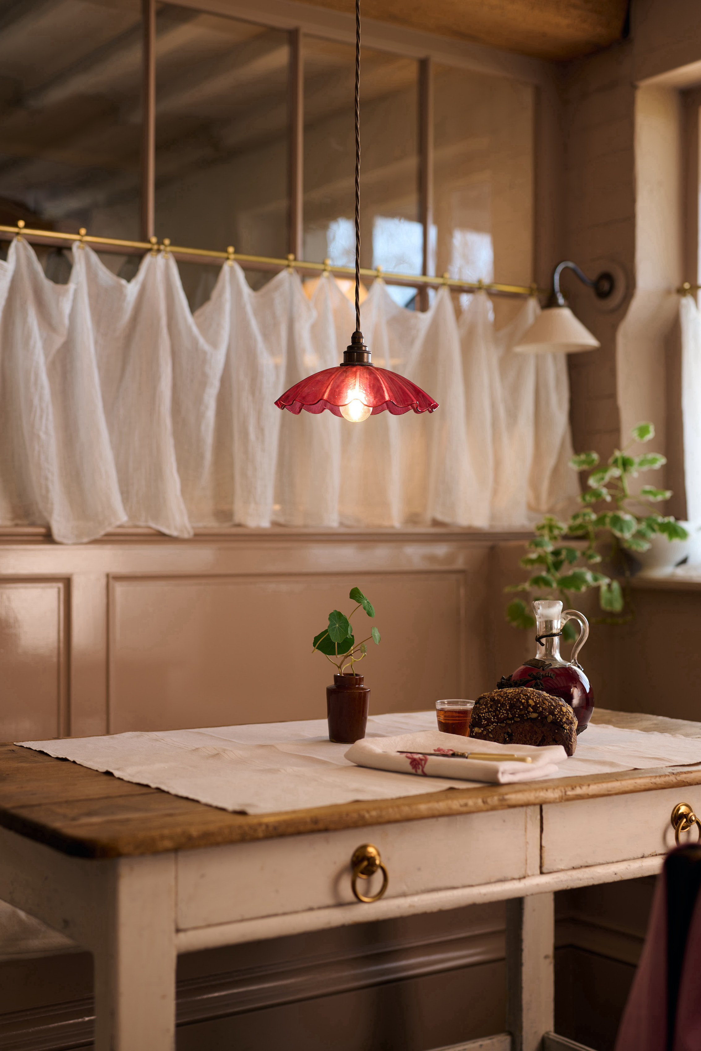 Warm kitchen interior with a red ruffled light fixture, white linen curtains, and natural wood textures.