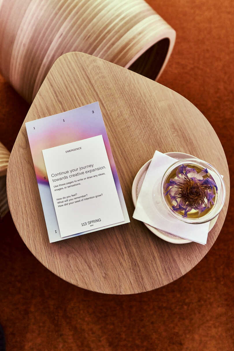 A cup of tea with flower petals and a motivational card on a small table.