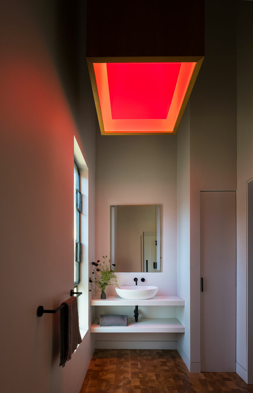 A bathroom sink area with a large ceiling panel glowing with a soft red light.