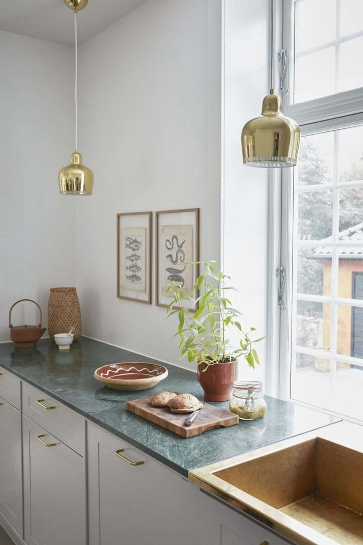 Scandinavian-style kitchen featuring a green stone countertop and white cabinetry with brass accents.