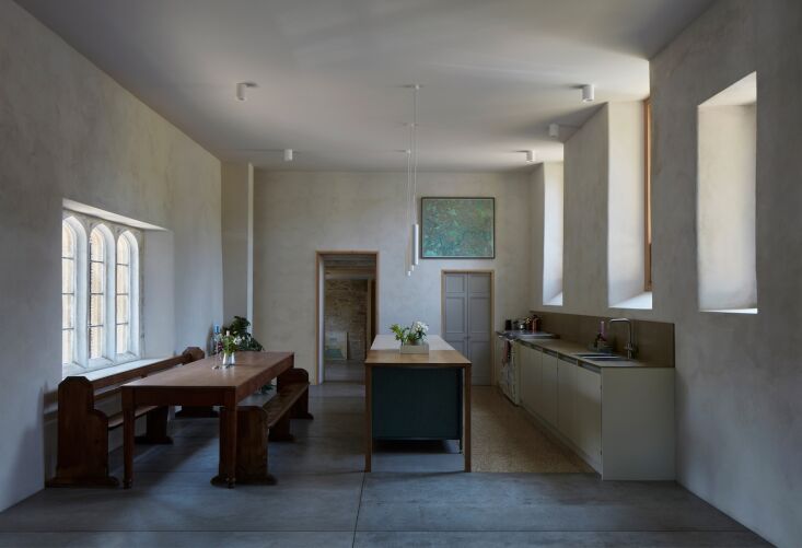 An open-plan kitchen and dining area featuring original Gothic windows from the 1580s and modern grey flooring.