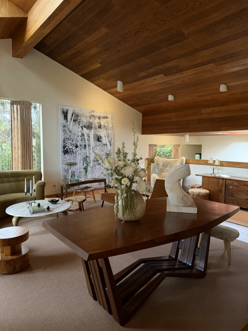 Mid-century modern living room featuring a wood-beamed ceiling, marble sculpture, and green velvet sofa.
