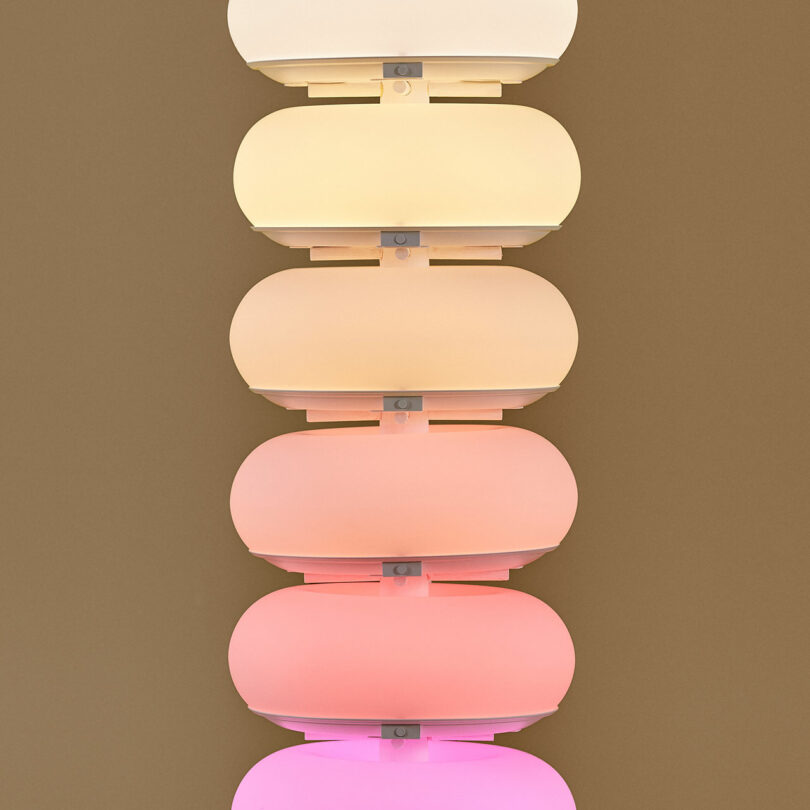 A stack of translucent circular light fixtures glowing with gradient colors on a dark wall.