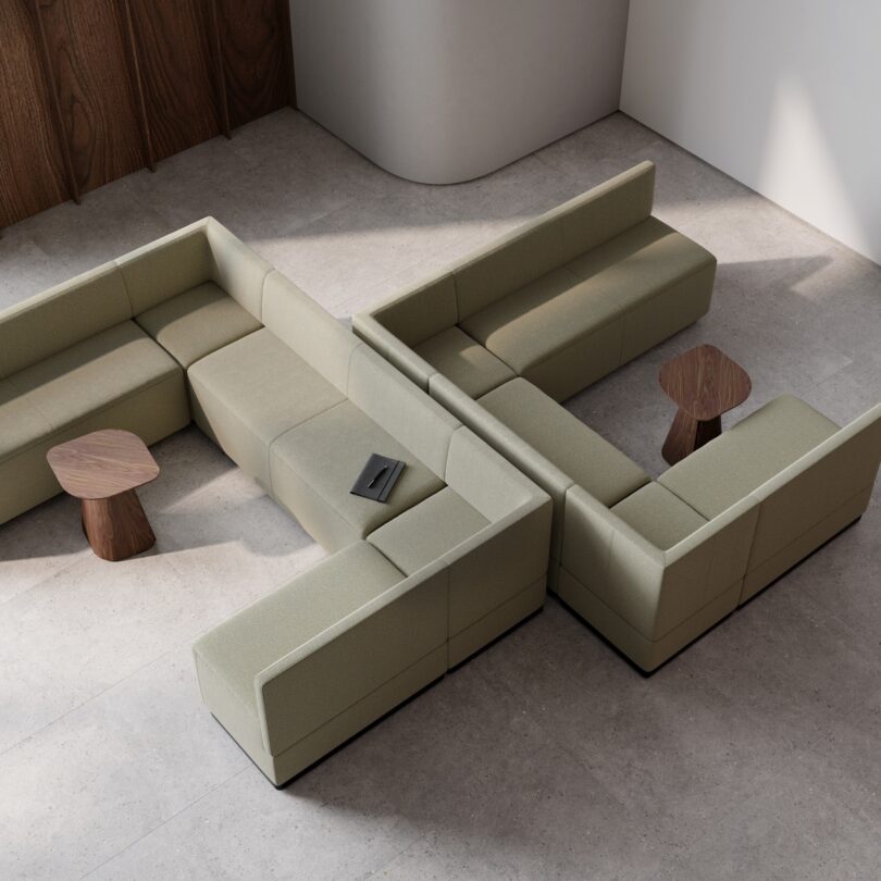 Aerial view of a modular green L-shaped sofa with small wooden side tables on a stone floor.