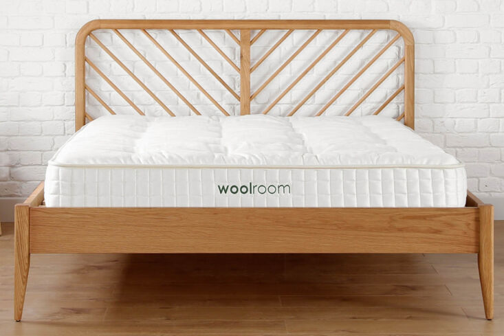 Modern bedroom with a white quilted Woolroom mattress set against a white brick wall and wooden floors.