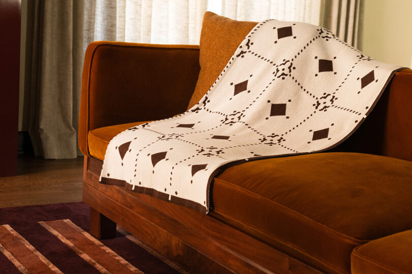 A patterned blanket on a rust-colored velvet sofa with a striped rug in a modern living room.