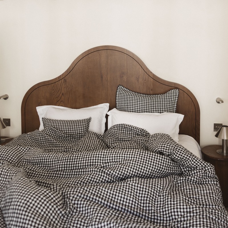 A modern bedroom with black-and-white gingham bedding and a wooden arched headboard.