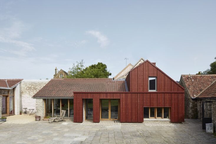 Modern building extension featuring red-stained timber cladding that complements the original stone structure and terracotta roof tiles.