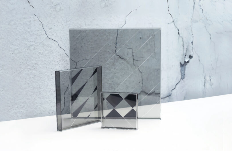 Lightware glass panels leaning against a textured, cracked concrete wall, casting sharp geometric shadows.