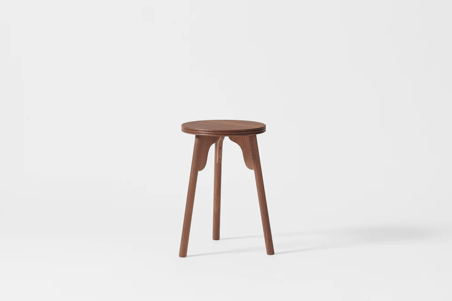 A simple three-leg walnut stool used as a bedside table.