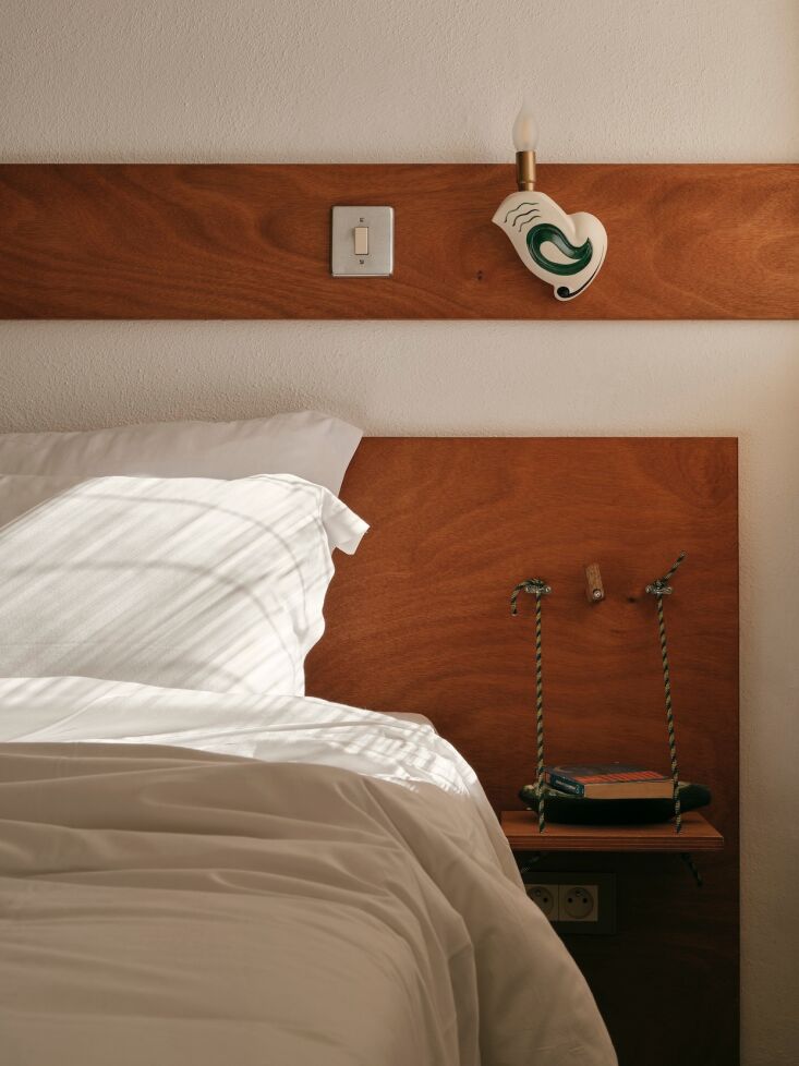 Close-up of a fold-down nightstand suspended by thin ropes with a wooden latch at the top.