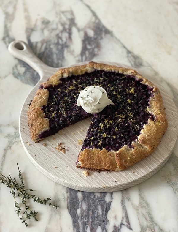 A rustic blueberry lemon thyme crostata with golden-brown crust and herb accents.