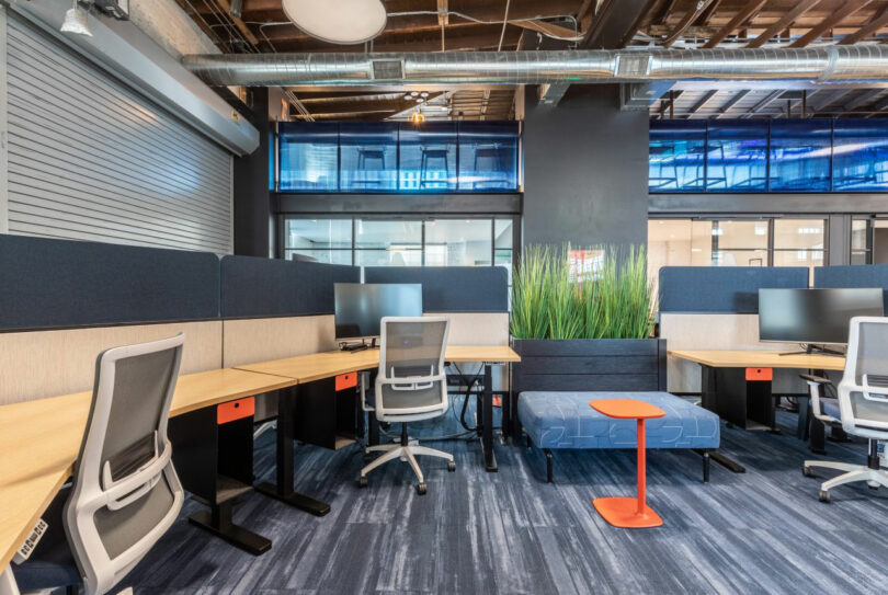 An open-plan office layout with modern workstations, blue partitions, and industrial overhead lighting.