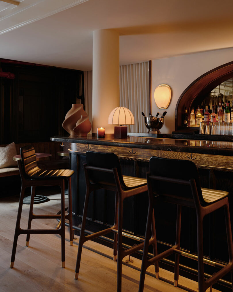 A dimly lit bar counter with high stools, curated spirits, and atmospheric lighting.
