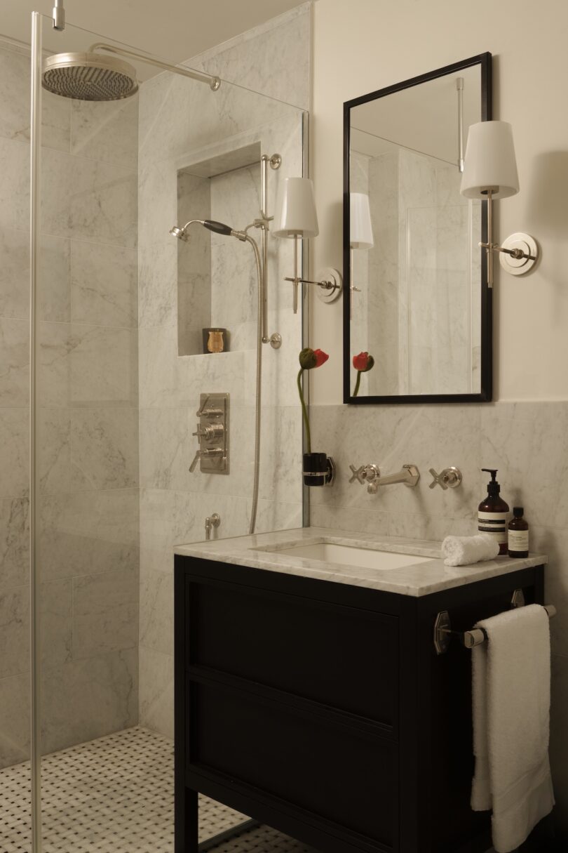 Modern bathroom with stone-clad walls, a black vanity with marble top, and elegant wall sconces.