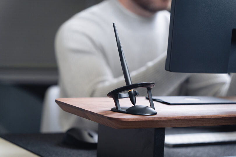 A Novium Hoverpen on a wooden desk next to a computer monitor in a bright, modern office.