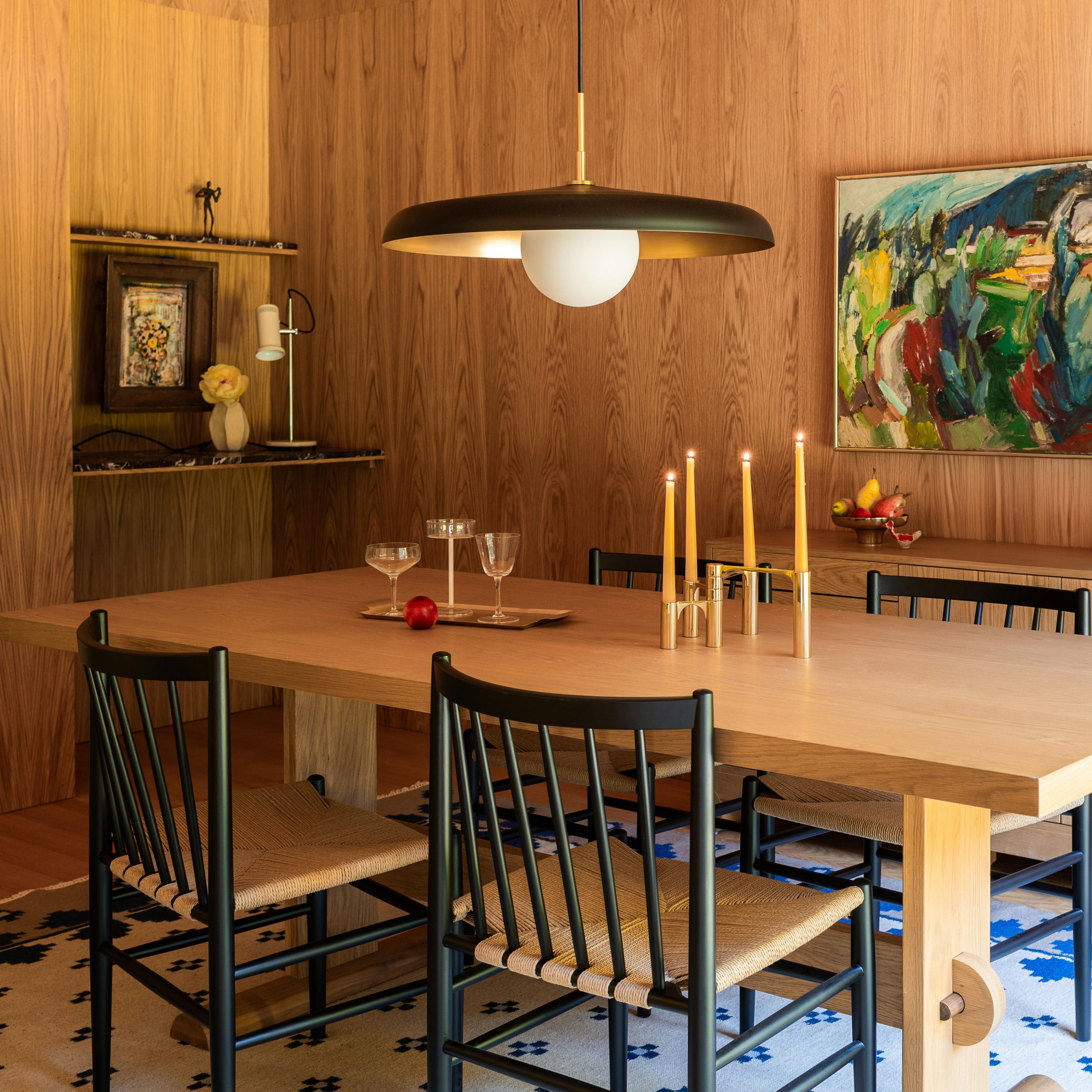 A black and brass hanging pendant light in a dining room with natural wood-paneled walls.