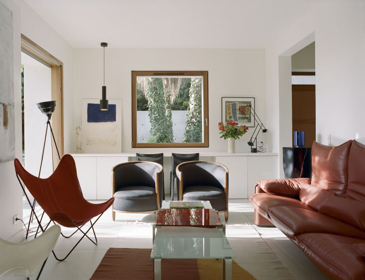A modern living room with a Maralunga sofa, Aalto pendant lights, and high ceilings with historic moldings.