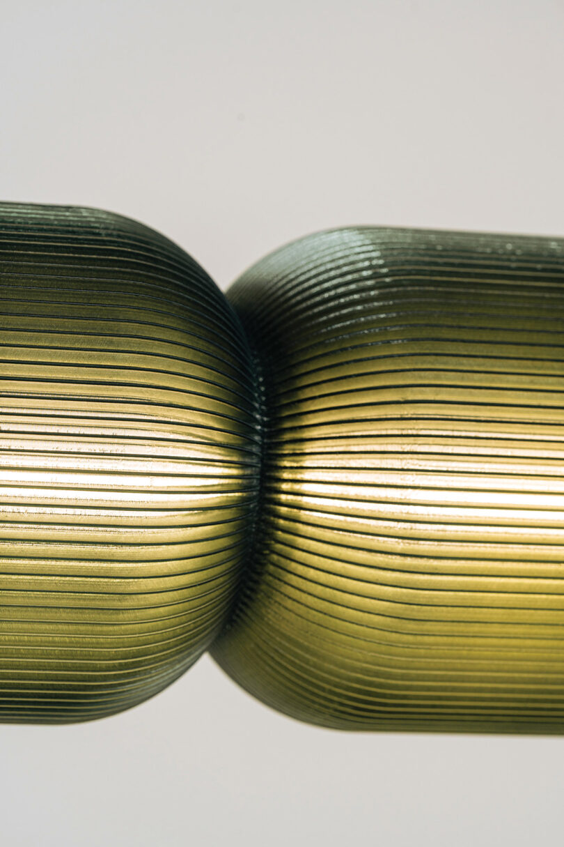 Macro view of two metallic-finish ribbed cylindrical light components touching.