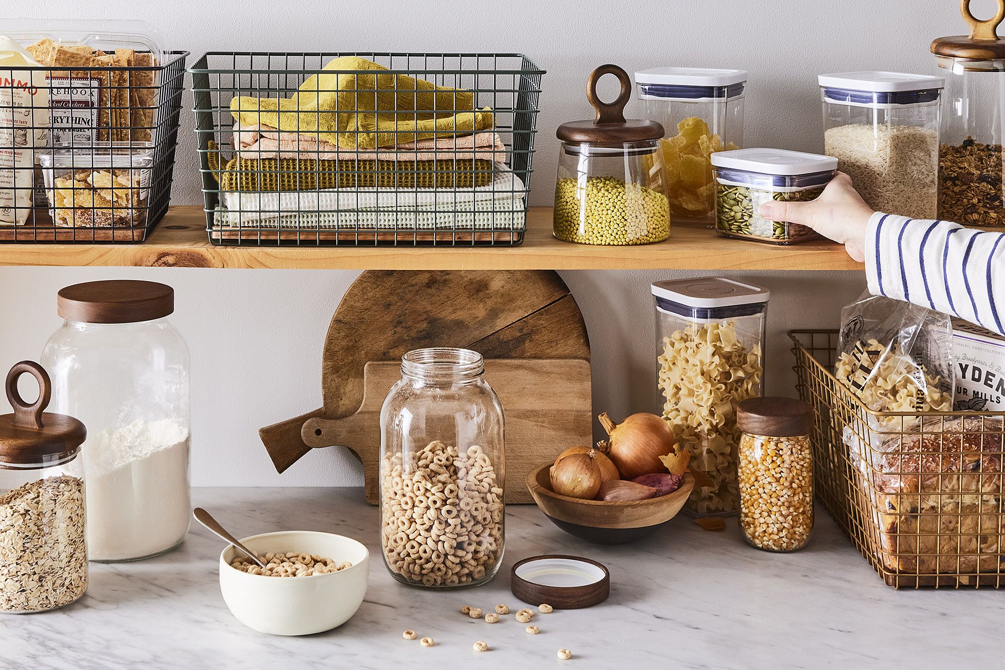 A well-organized kitchen pantry with wooden shelves, glass jars for dry goods, and wire baskets for snacks.