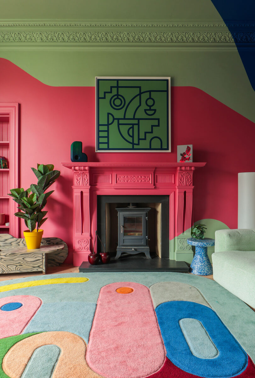 A maximalist living room with a pink fireplace, green walls, and a multi-colored geometric rug.
