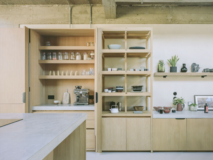 Modern kitchen featuring light oak cabinets and a raw concrete ceiling, representing a blend of natural and industrial materials.