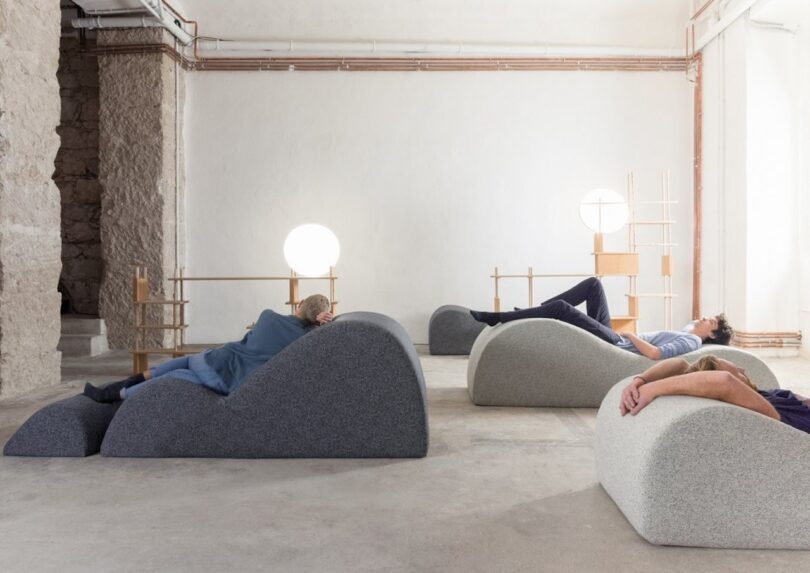 People resting on uniquely shaped cushioned foam furniture in a minimalist office setting.