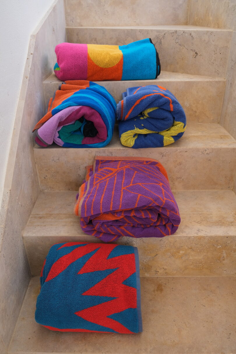 A collection of colorful patterned towels arranged on a minimalist beige stone staircase.