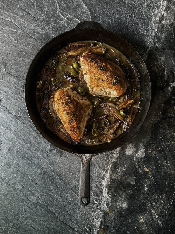 Chicken thighs searing skin-side down in a white enameled cast iron skillet.
