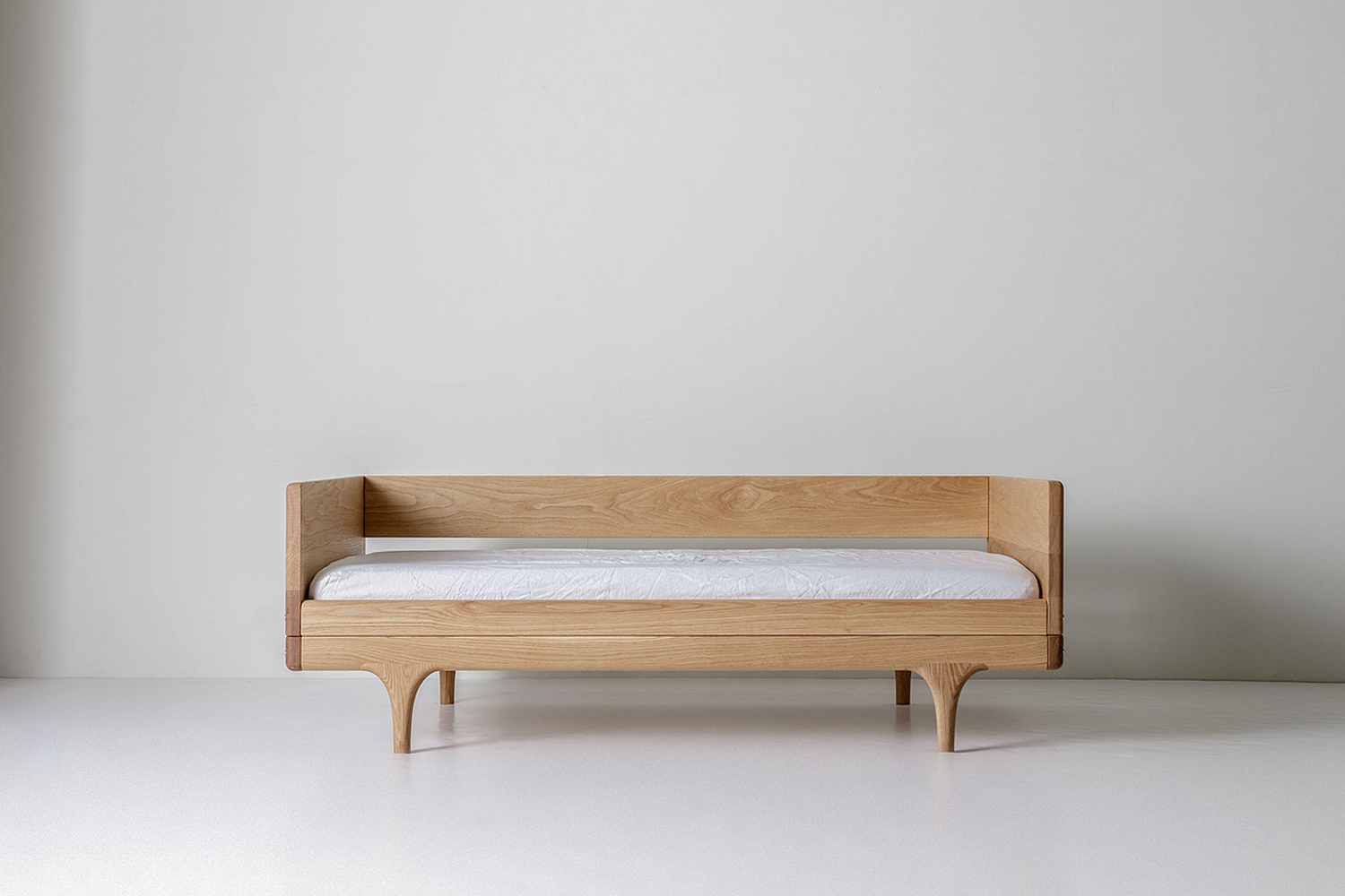 A minimalist wooden divan-style junior bed with clean lines and sculpted legs.