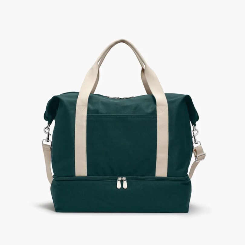 A dark green canvas weekender bag with white handles and a shoulder strap.