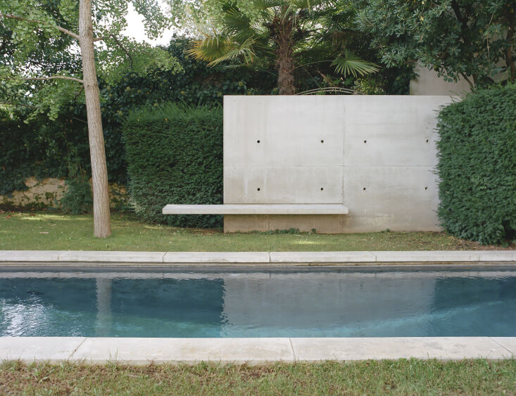A modern backyard swimming pool with concrete coping that mimics the texture of natural stone.