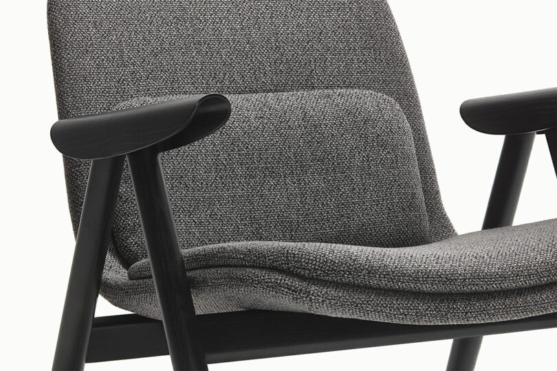 Detailed close-up of a Hout chair featuring textured gray fabric and smooth dark wood armrests.