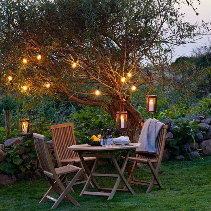 Outdoor patio scene at dusk with Scandinavian design wooden furniture and warm hanging lanterns.