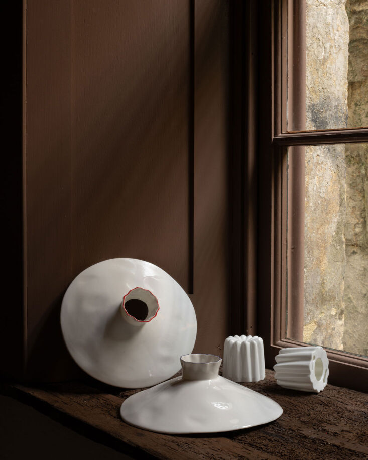 Hand-crafted white bone china ceramics with organic profiles on a wooden windowsill.
