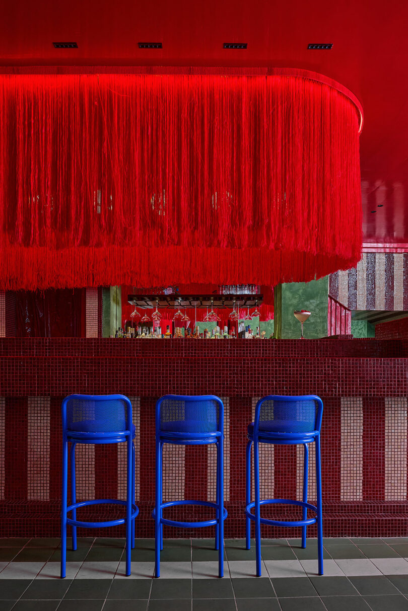 A bar interior featuring a red tiled counter and a dramatic red fringe installation hanging from the ceiling.