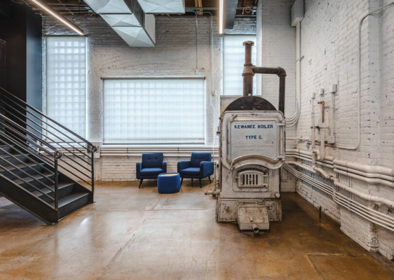 A vintage blue Kewanee boiler preserved as a decorative element in a modern office lounge with exposed white brick walls.