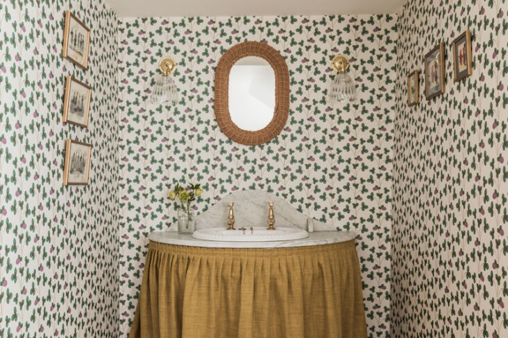 An ochre linen curtain wrapped around a vintage marble sink in a rustic bathroom.