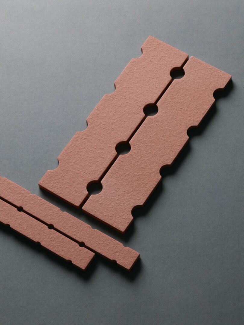 Close-up of reddish-brown porcelain tiles with interlocking notches and circular cutouts.
