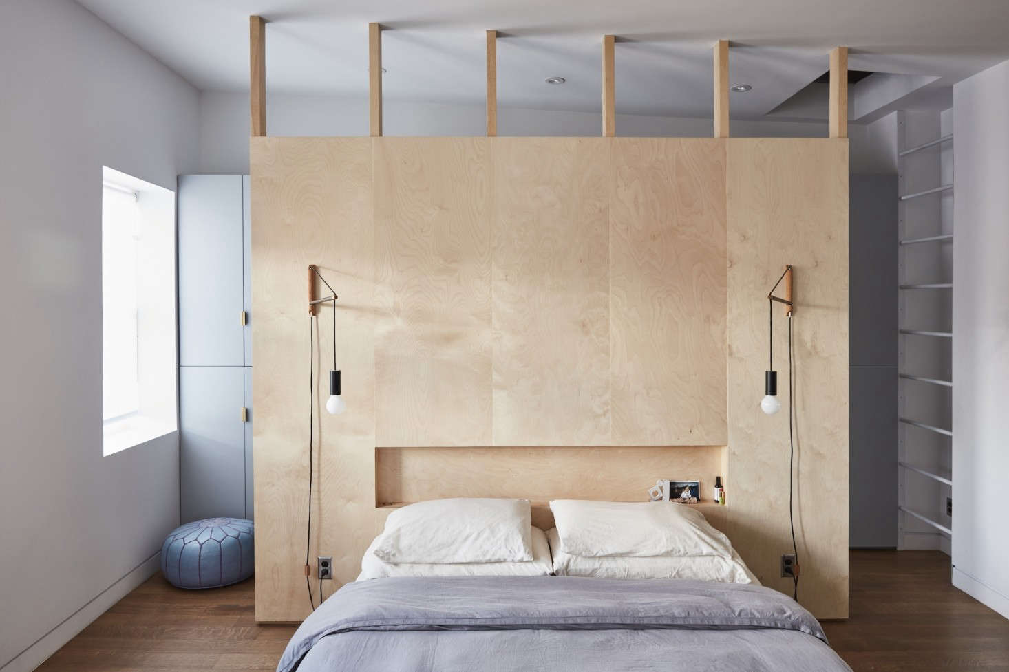 Modern bedroom with a custom plywood headboard featuring integrated lighting and minimalist Scandinavian styling.
