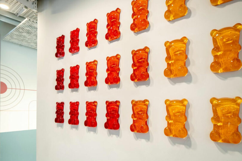 Minimalist white wall decorated with rows of red and orange glossy gummy bear sculptures.