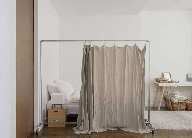 A private sleeping area delineated by a rolling clothing rack and a white curtain.