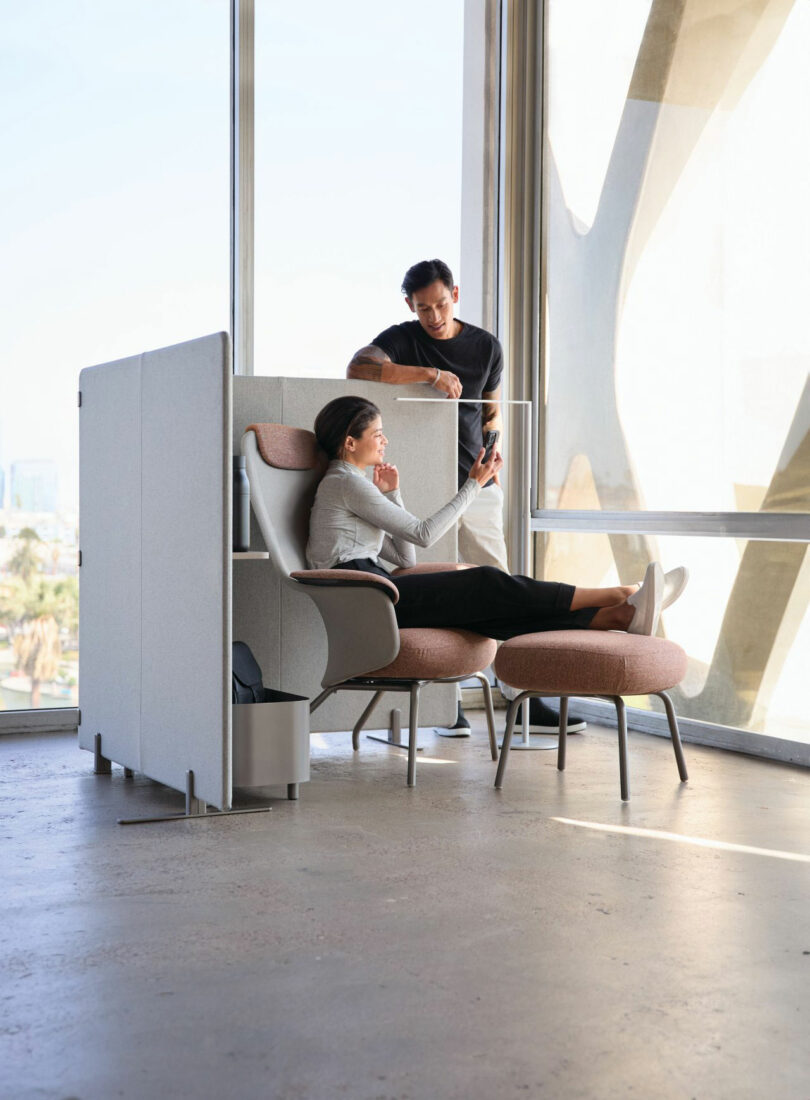 Two people talking in a modern office lounge with minimalist furniture and acoustic partitions.