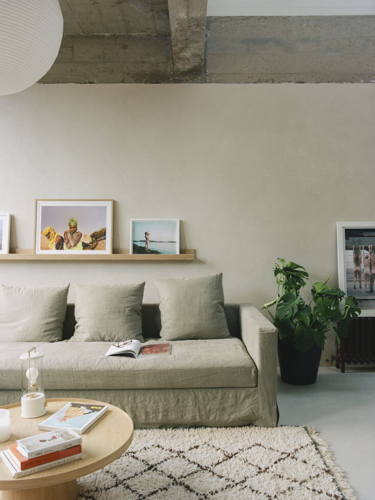 Minimalist living room with a neutral sofa, wooden shelf, and soft lighting under a concrete ceiling.