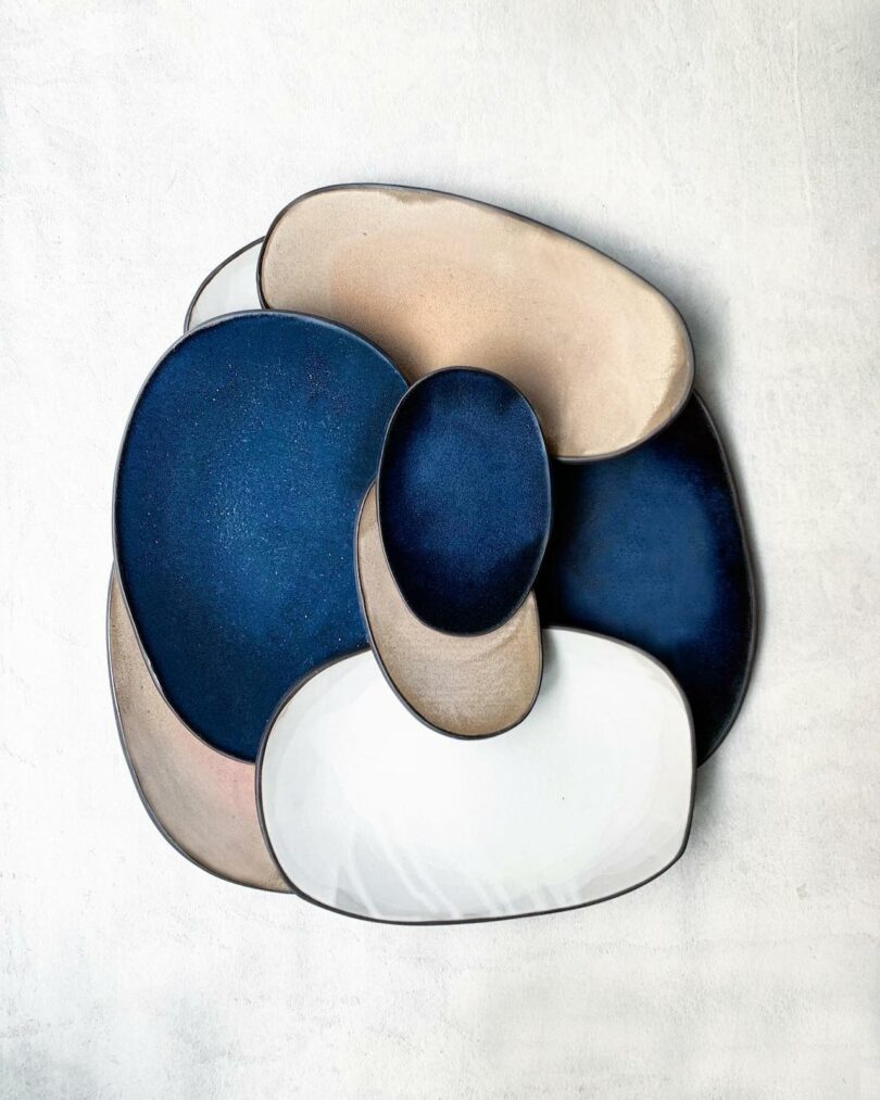 Abstract ceramic plate set in navy blue, beige, and white on a textured surface.