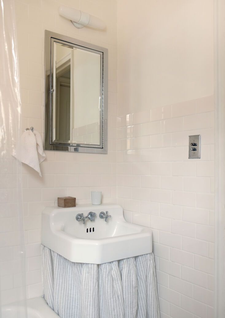 A small bathroom featuring a striped duster skirt under a pedestal sink with white subway tiles.