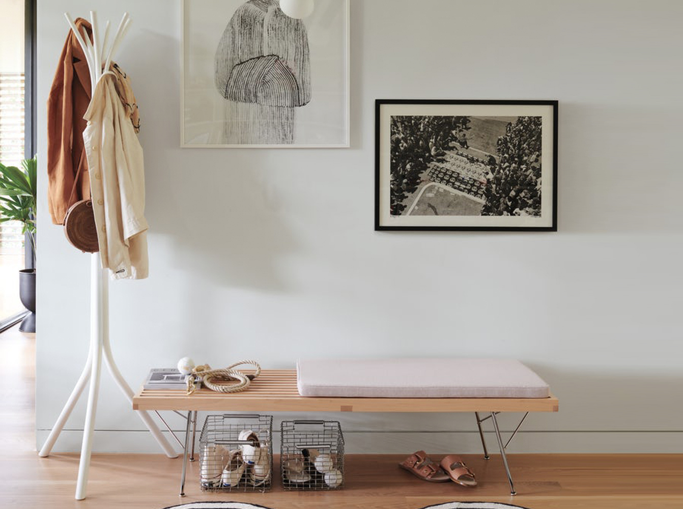 Modern entryway with a white coat rack, wooden bench, and organized shoe baskets.