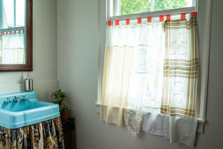 A bathroom with a sink skirt and curtains made from various stitched-together fabric scraps.