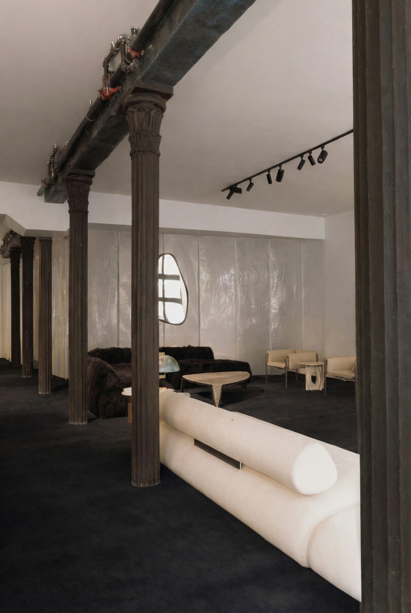 Industrial-chic living space with dark wood columns, black carpet, and modern cream sofas.